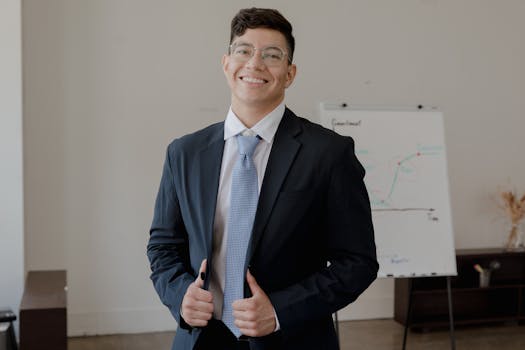 Smiling businessman in formal attire standing confidently in an office with a whiteboard.