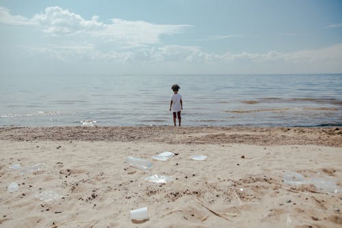 Child in White Shirt and Black Shorts Standing on Beach Shore