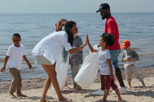 Free A diverse group of volunteers, including children and adults, clean up a beach and celebrate with high-fives. Stock Photo