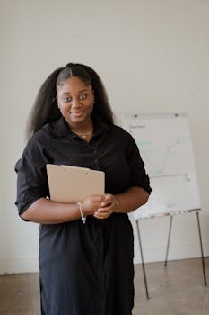 African American woman presenting in office environment with clipboard and whiteboard.