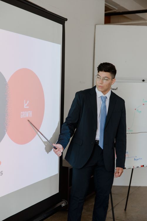 Free Businessman in a suit presenting a growth strategy using a pointer on a projector screen. Stock Photo