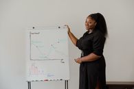Woman in Black T-shirt and Brown Skirt Standing in Front of Whiteboard