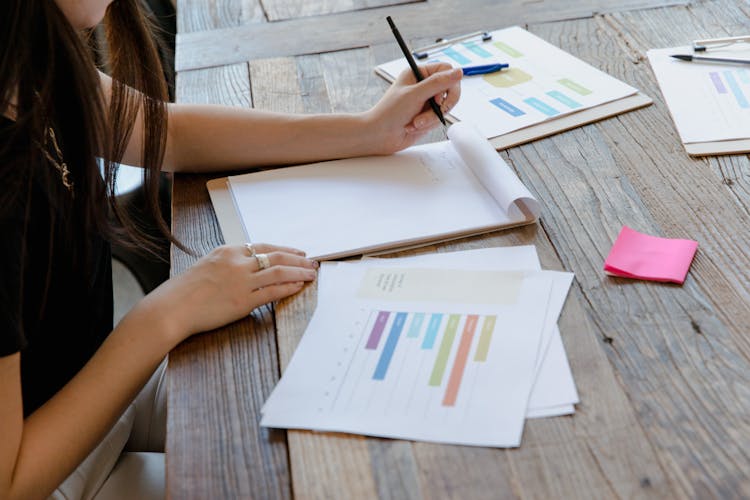 A Person Taking Notes While Looking At Documents