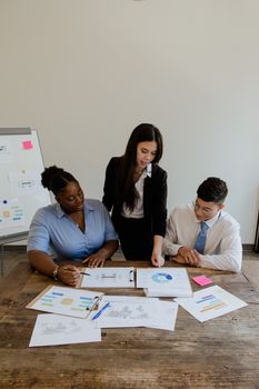 A focused business team engages in a meeting, discussing charts and graphs around a wooden table.