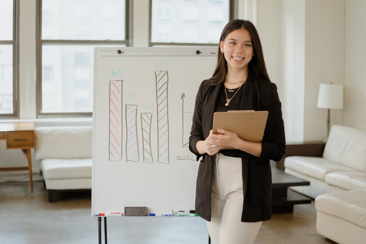 Woman In Black Blazer Standing Beside A Whiteboard With Graphs