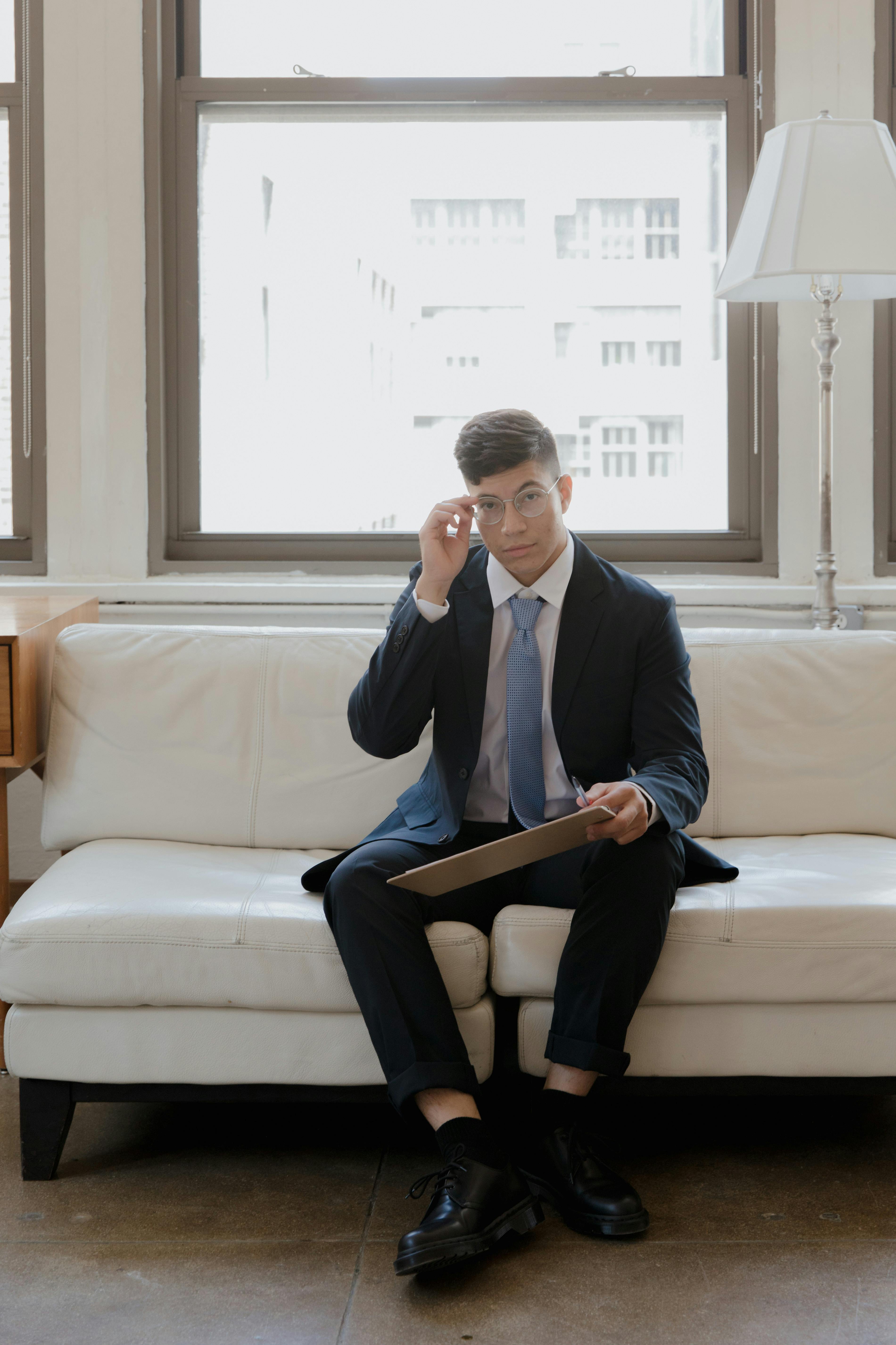 Businessman sitting on a white couch holding a folder, emphasizing a professional work setting.