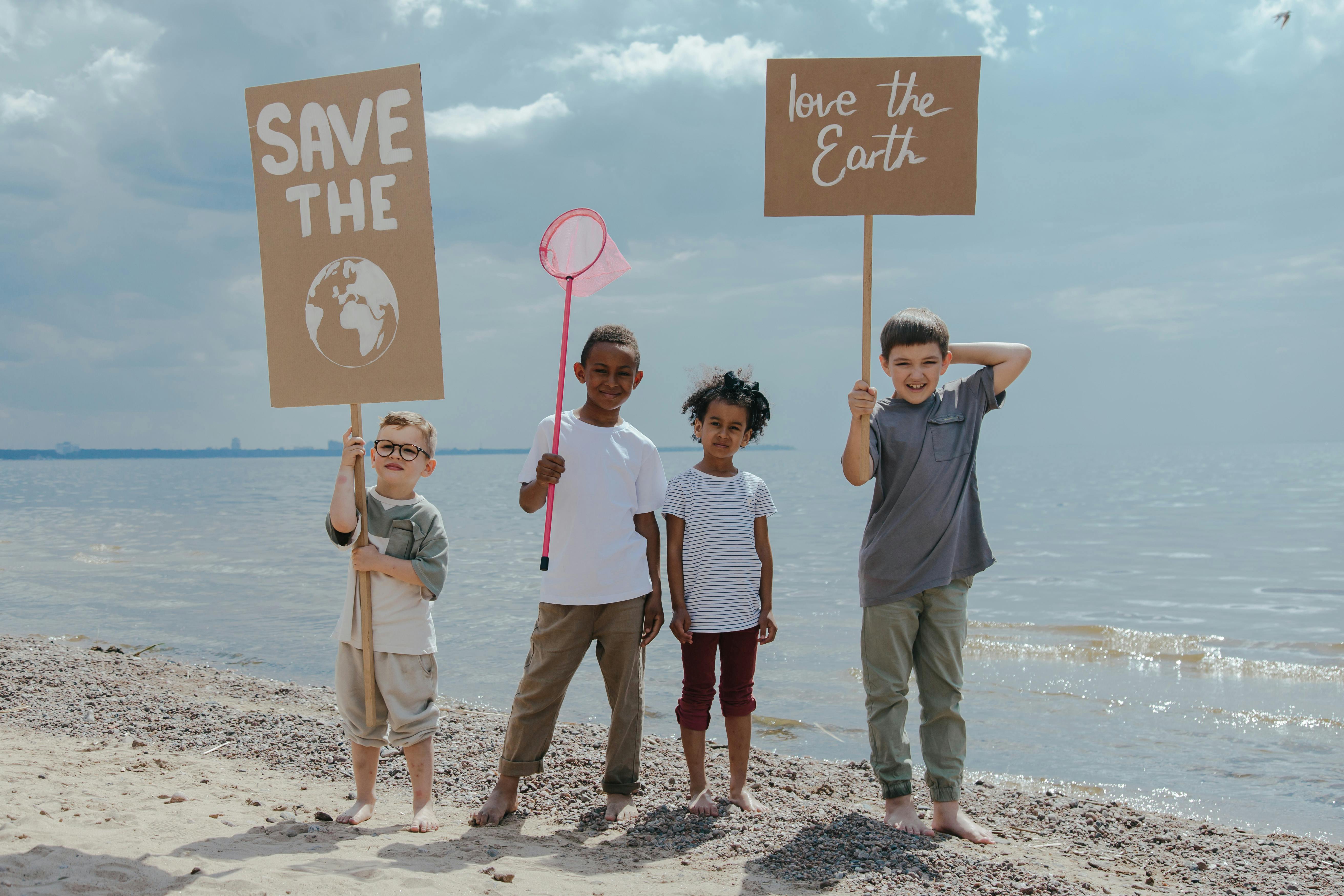 children standing at the seashore while holding signages