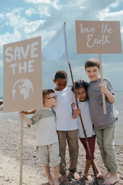 Children Standing at the Seashore while Holding Signages