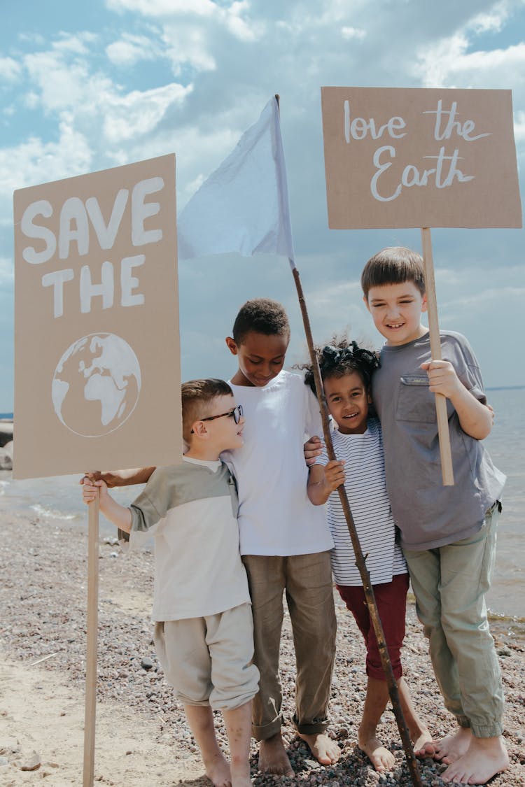 Children Standing At The Seashore While Holding Signages