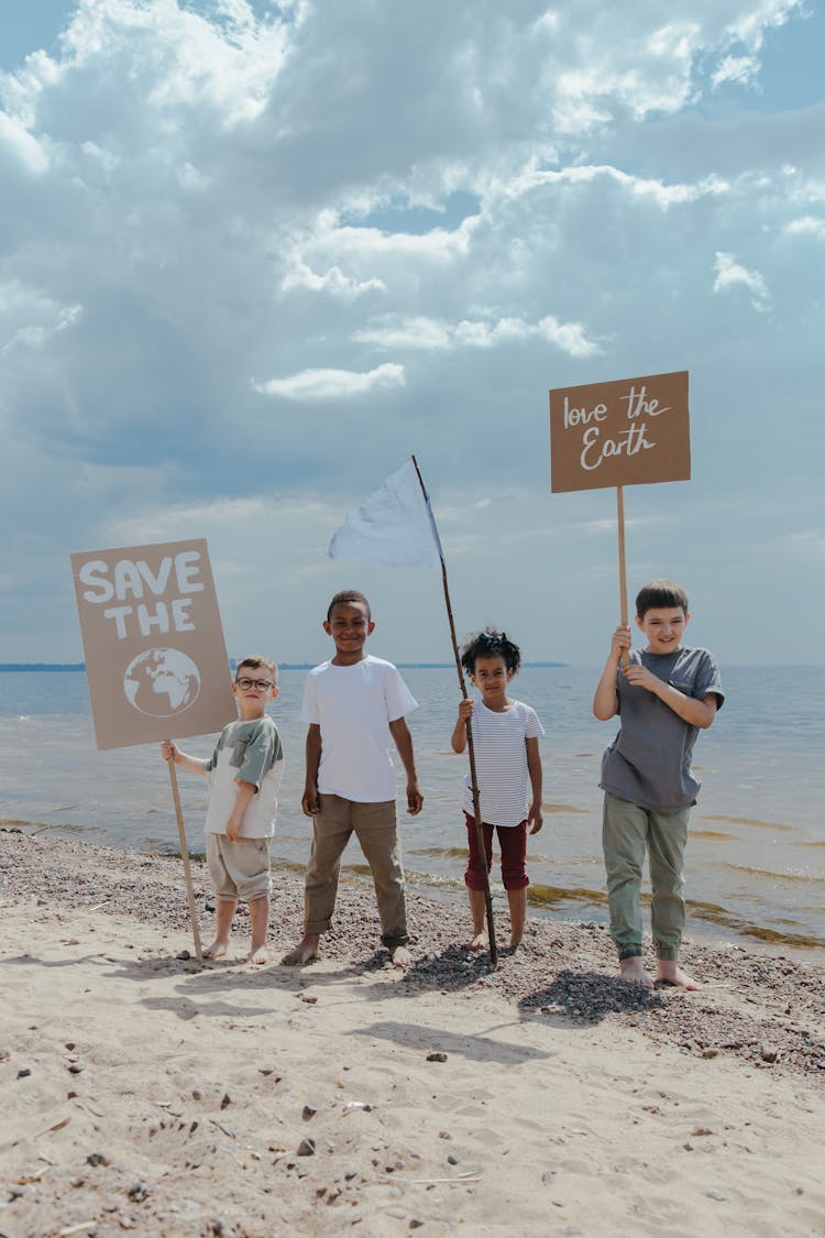 Children Standing At The Seashore While Holding Signages