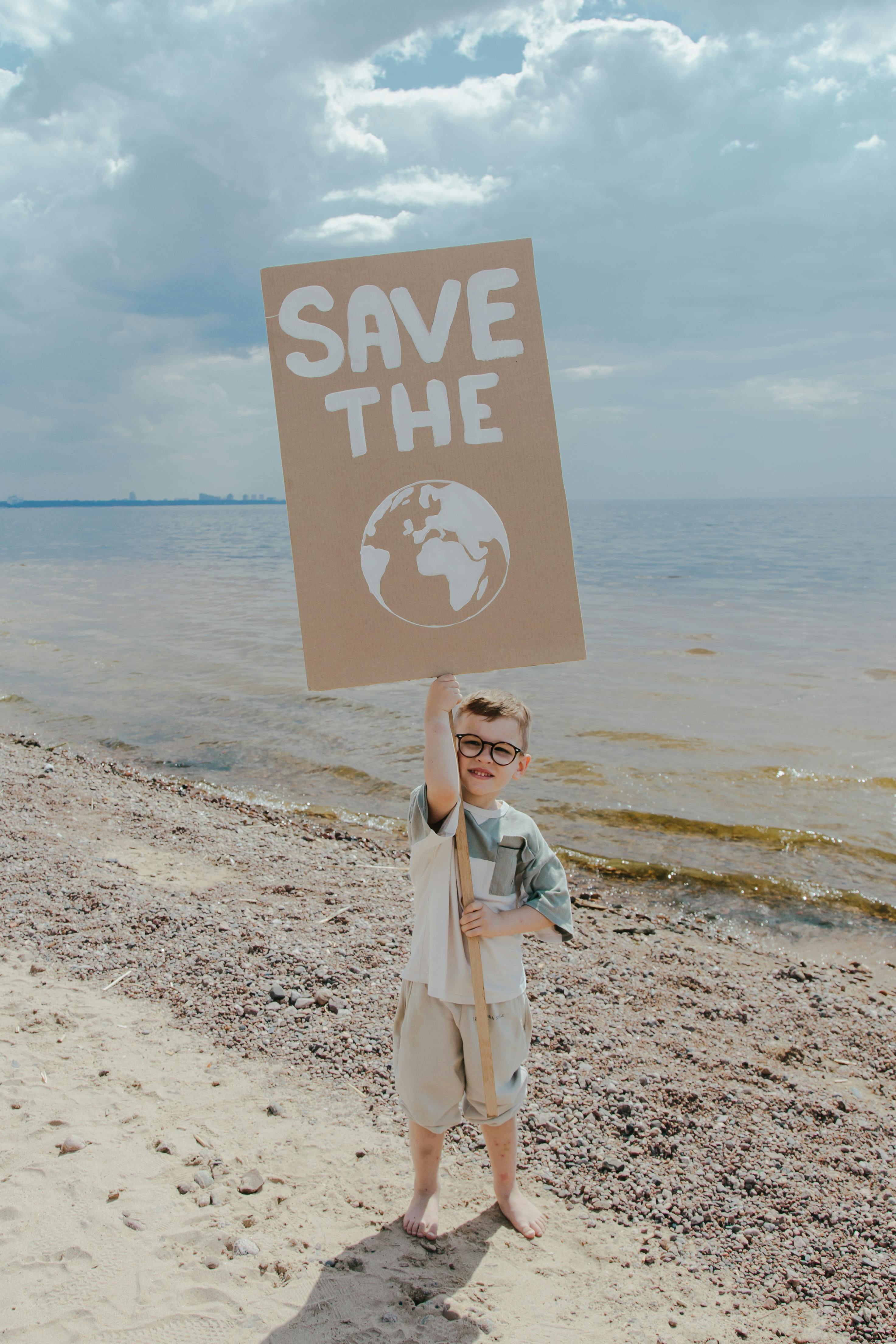 a boy standing at the seashore while holding a signage