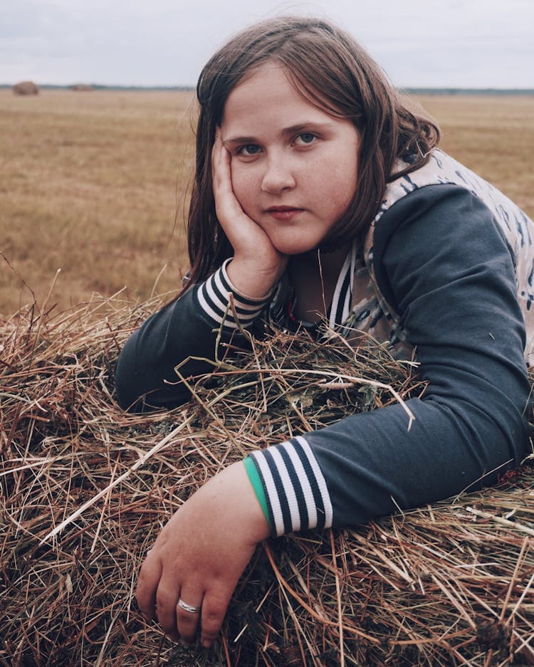 Woman Leaning Forward On Haystack With Hand On Cheek 