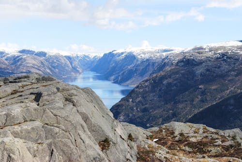 Breathtaking view of calm cold lake surrounded with rocky hills covered with snow under blue sky