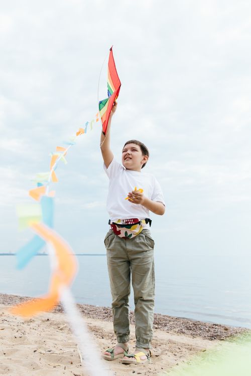 Free Young boy joyfully flies a colorful kite on a sandy beach, capturing a moment of seaside recreation. Stock Photo