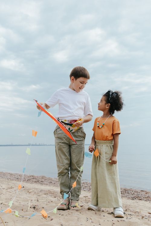Free Two children playing with a colorful kite on a sandy beach, enjoying a day outdoors. Stock Photo