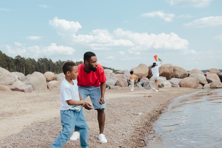 A Man And A Young Boy Throwing Rocks On Water