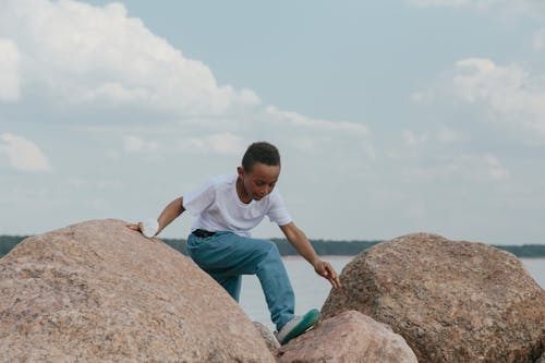 A Young Boy in White T-shirt and Blue Denim Jeans Climbing on Rocks