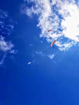 Three paragliders soaring against a vivid blue sky with fluffy clouds.