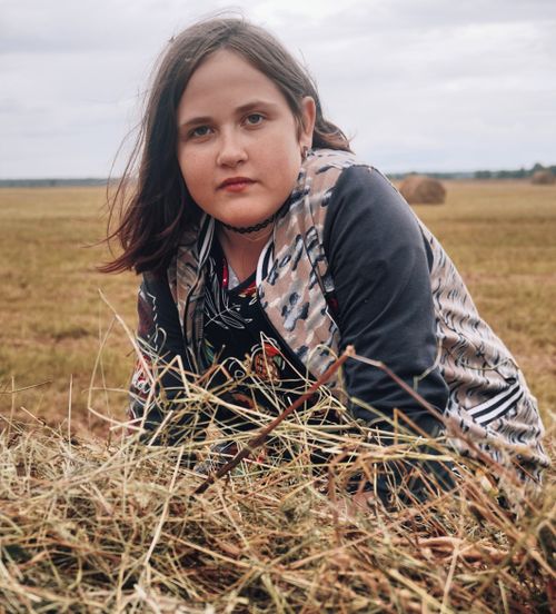 Free A young girl in a field wearing a choker and jacket, surrounded by hay bales. Stock Photo