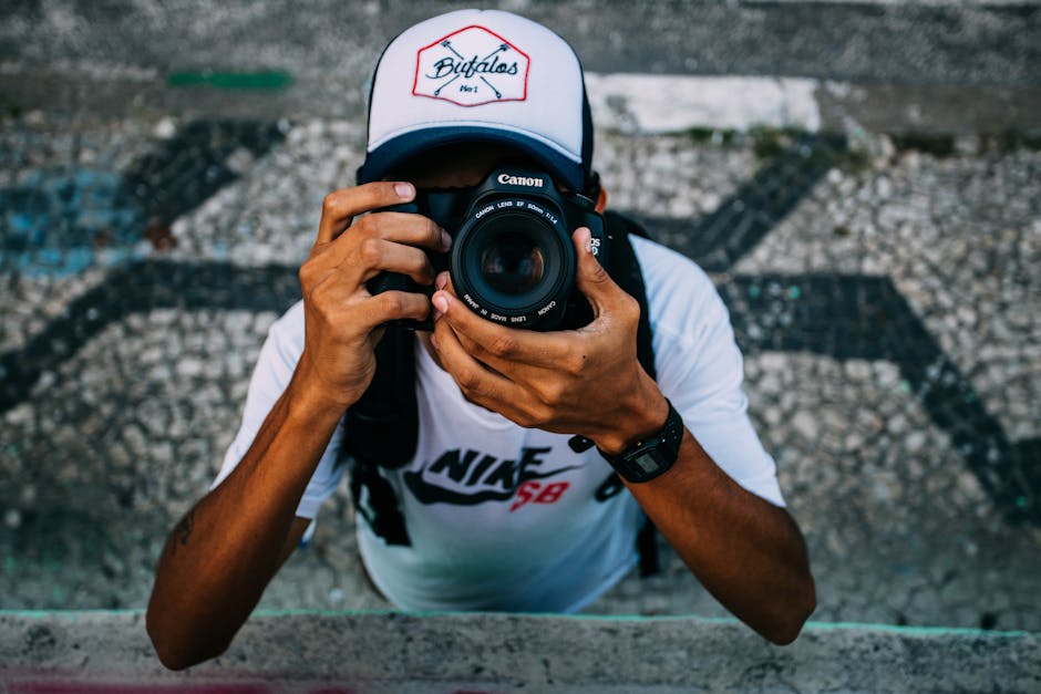 Man Wearing White Nike Sb Shirt Holding Black Dslr Camera