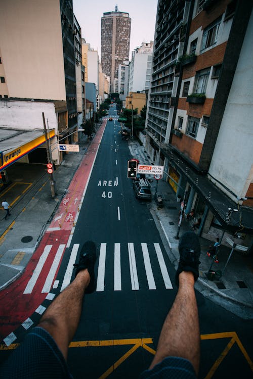 Person Wearing Black Lace Up Sneakers Facing Gray Concrete Road Top Between Concrete Buldings