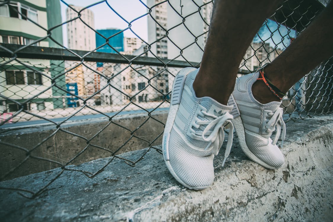 Person Wearing White Adidas Low Top Shoe Near Gray Cyclone Fence