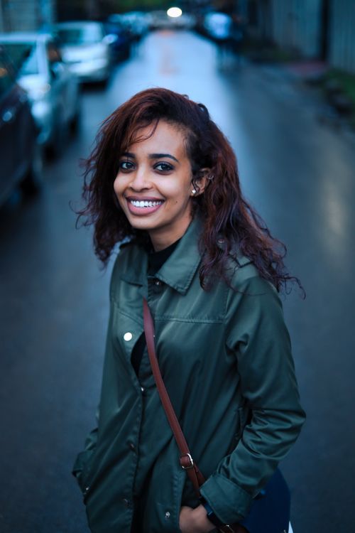 Free Young woman in a green jacket smiling confidently on a rainy urban street. Stock Photo