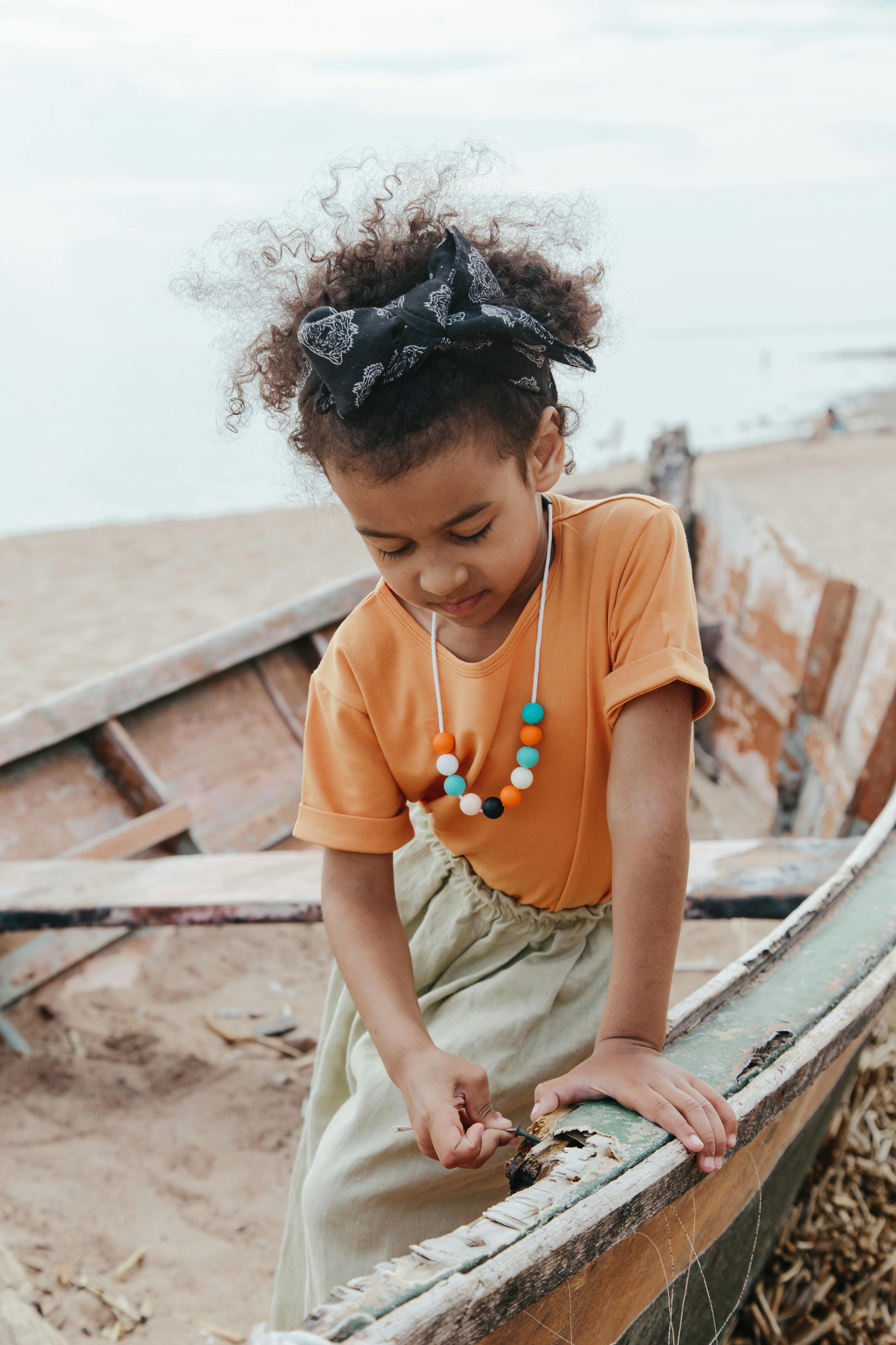 Young girl curiously exploring an old boat on a sandy beach, showcasing childhood innocence and wonder.
