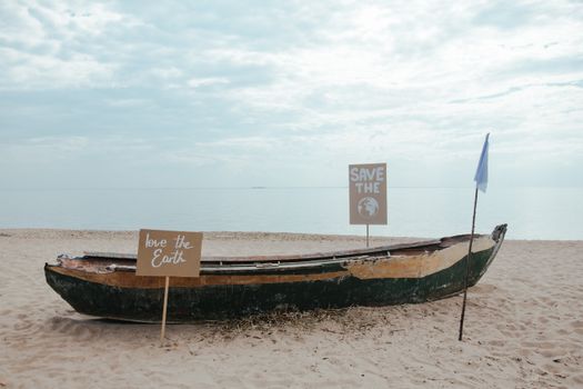 Weathered boat on beach with environmental signs advocating for planet protection.
