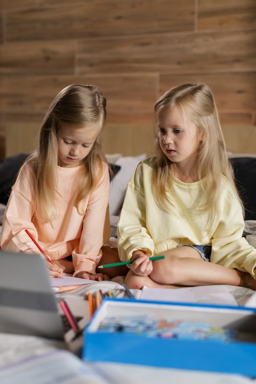 Free Two blonde sisters engage in drawing with colored pencils, sitting indoors. Stock Photo