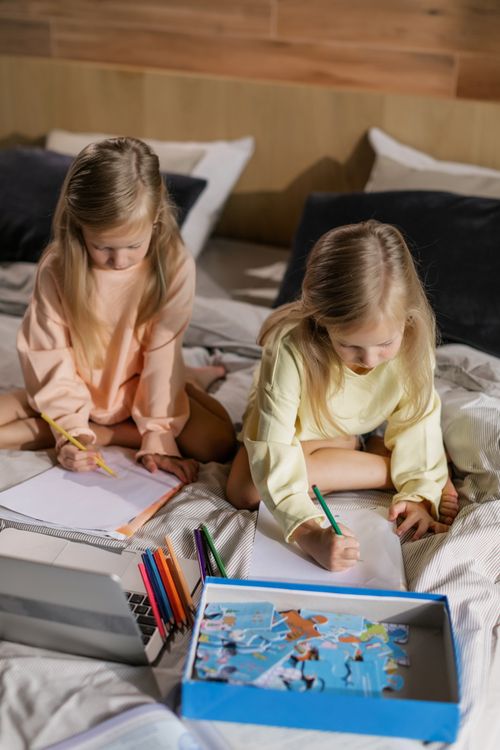 Free Two young girls drawing on bed with pencils and paper during an indoor learning activity. Stock Photo