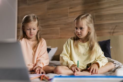 Free Two young girls sitting indoors learning online with a laptop in a cozy home setting, focused and engaged. Stock Photo