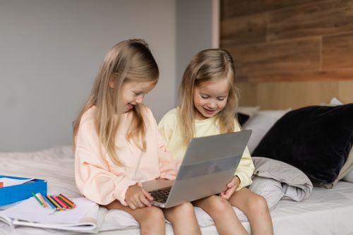 Free Two young girls engaged in online learning on a laptop while sitting on a cozy bed. Stock Photo