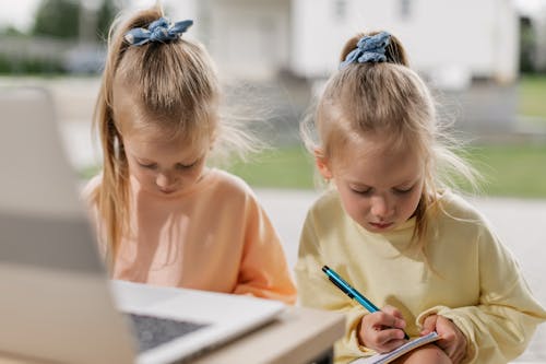 Free Close-Up Shot of Two Girls Having an Online Class while Writing Stock Photo