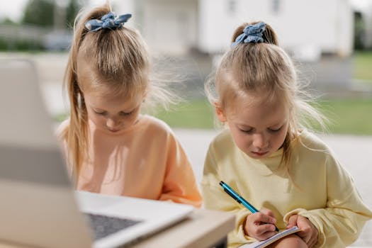 Two young girls focusing on online education using a laptop in a sunny outdoor setting.