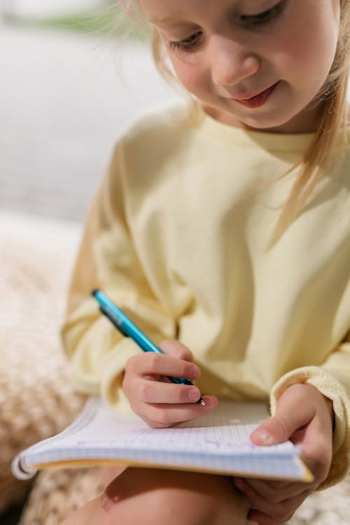 Girl in Yellow Long Sleeve Shirt Writing on White Paper