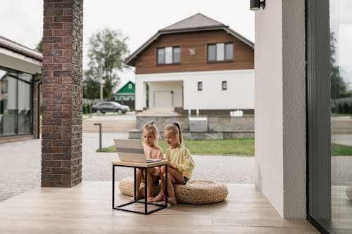 Girls Watching on Laptop while Sitting on Brown Woven Ottoman