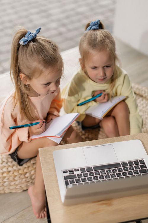 Free Two young girls focus on online lessons, writing in notebooks during a virtual class. Stock Photo