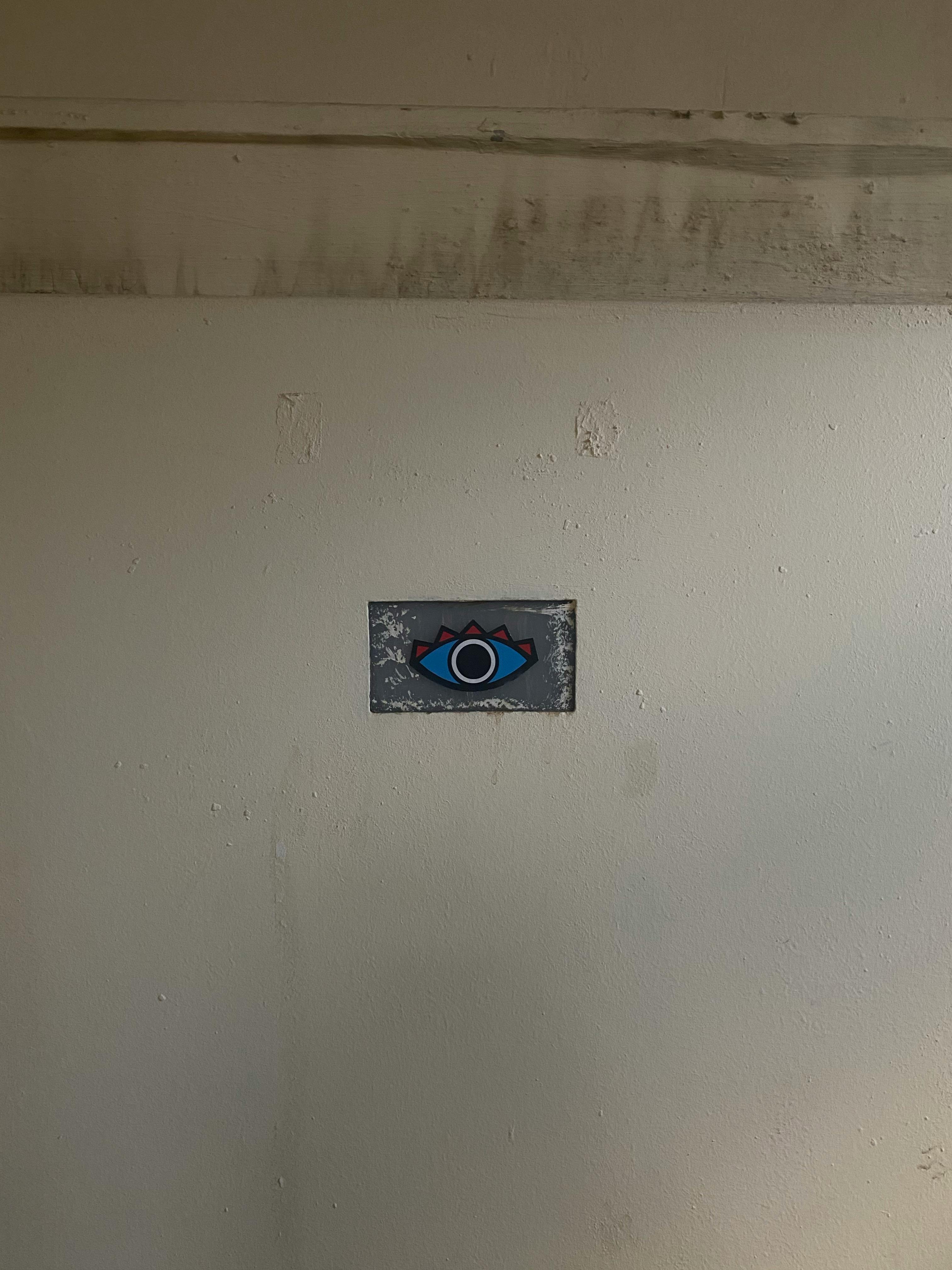 A small, abstract eye painting on a textured wall, offering a minimalist design.