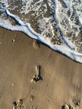 A gentle wave approaches a footprint on the sandy beach, capturing a serene coastal moment.