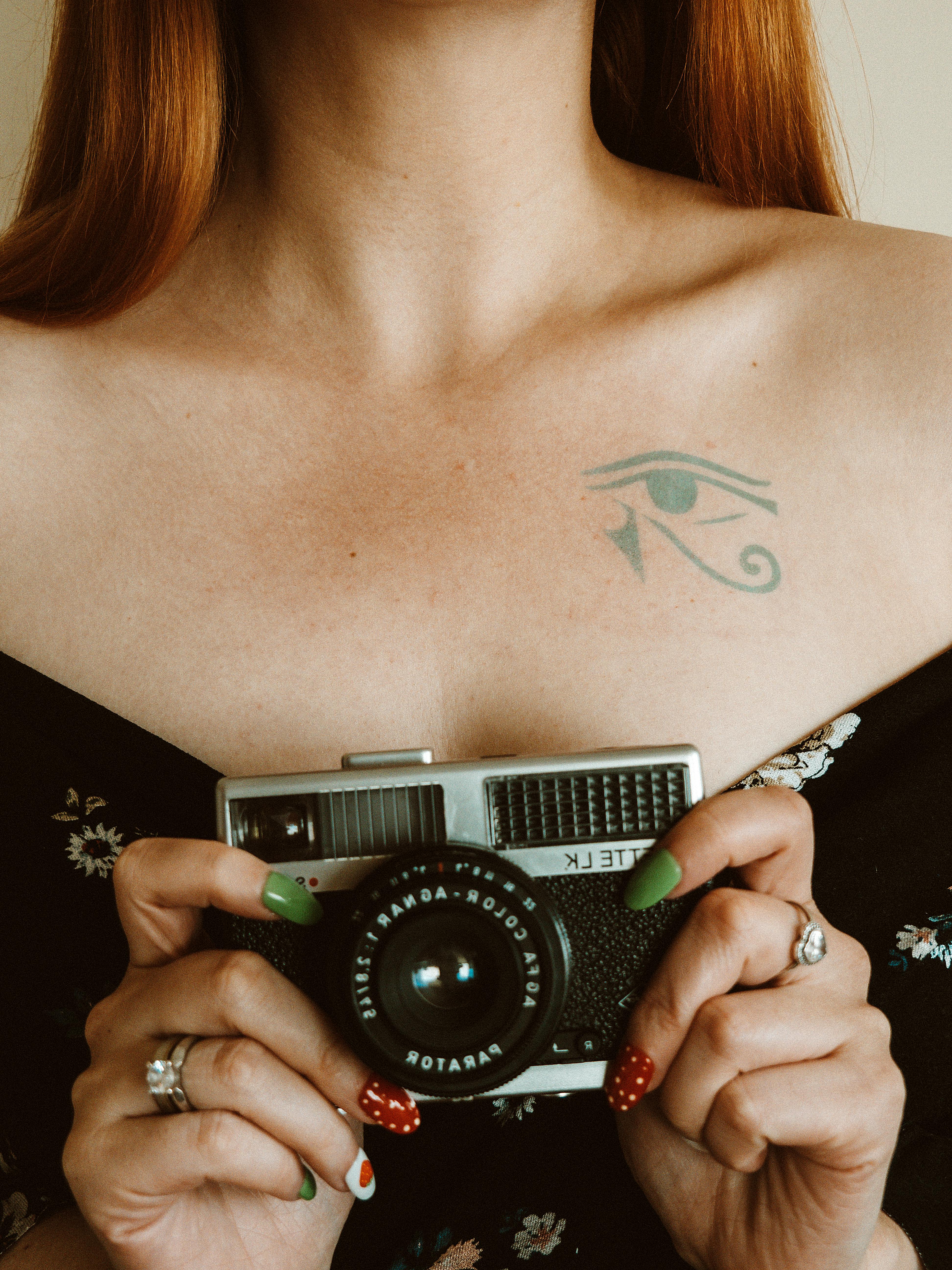 Close-up of a woman holding a vintage camera, showcasing her tattoo and colorful nail art for a creative aesthetic.