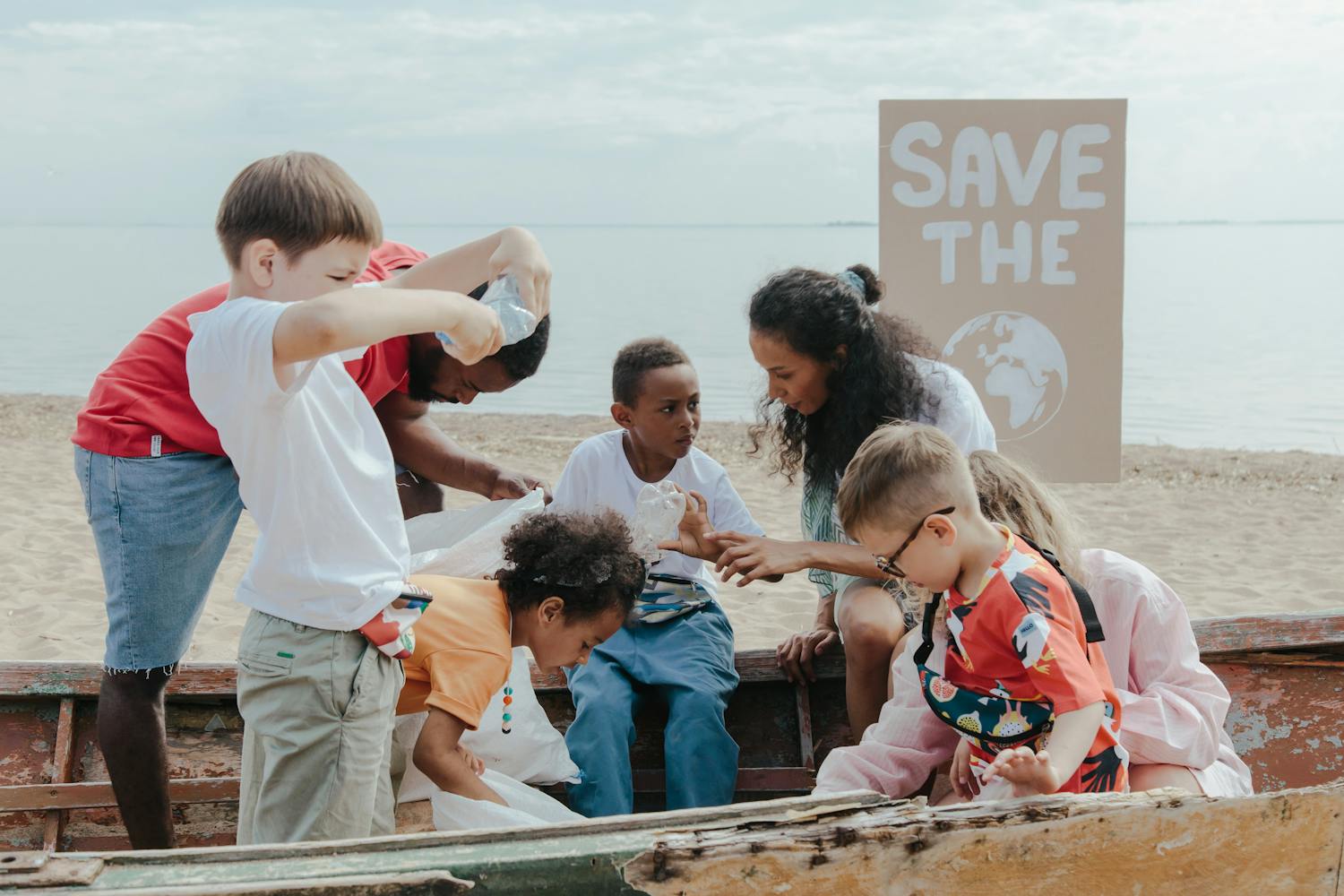 A group of children volunteering to clean a beach with a 'Save the Earth' sign.