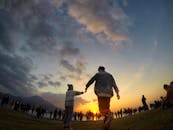 一对夫妇牵着手，在充满活力的日落天空下，背景中映衬着人群