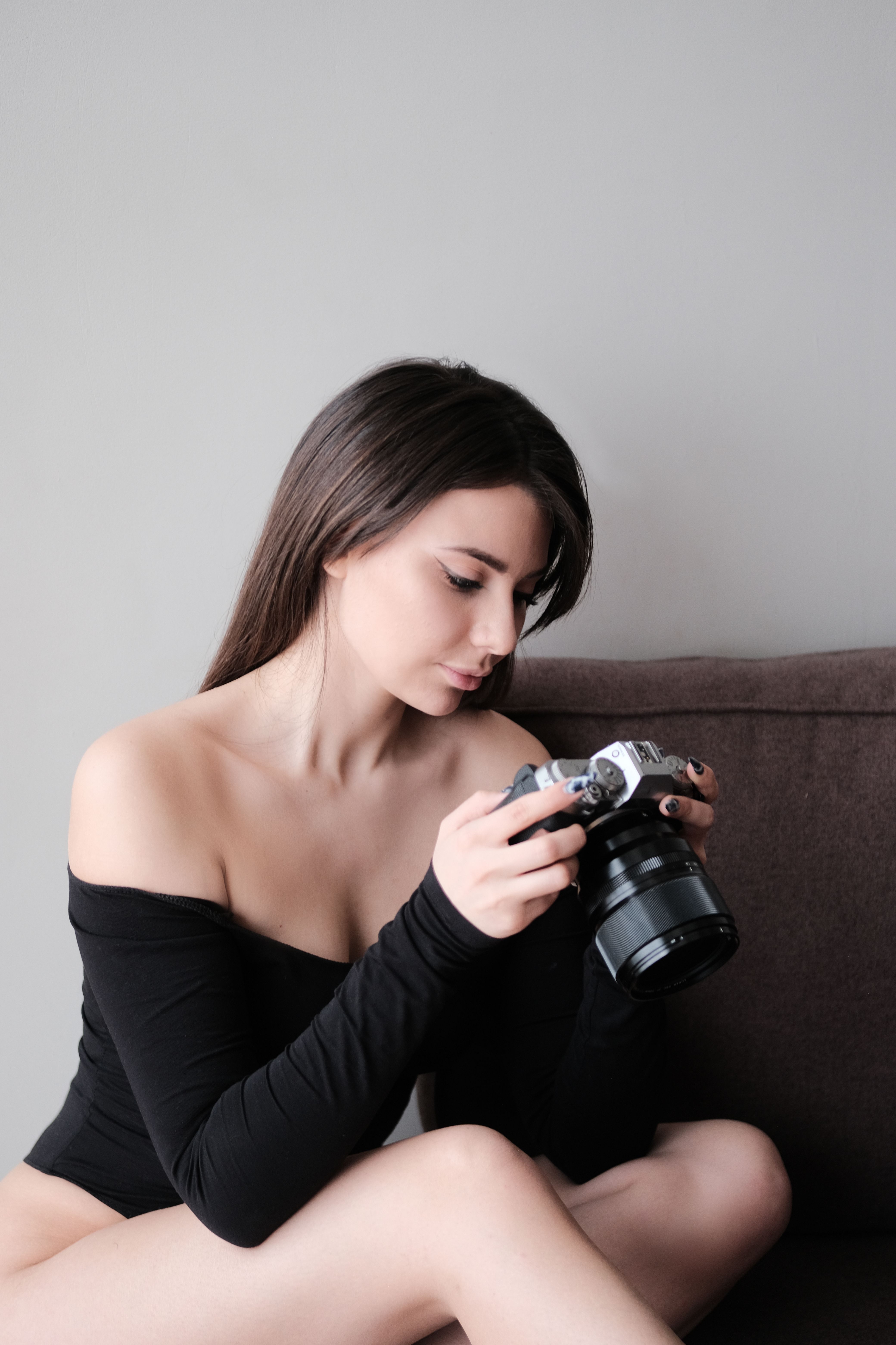 A woman in an off-shoulder top observes a camera in an artistic indoor setting.