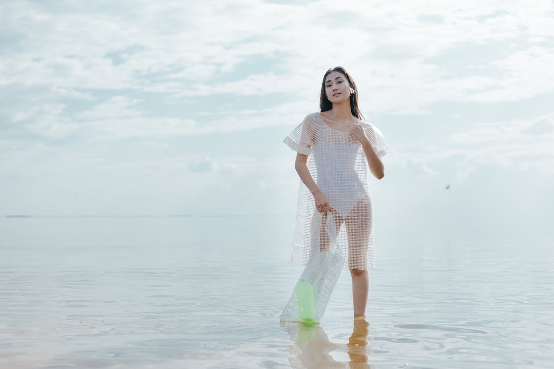 A Woman in White Bikini and See-Through Dress Standing in Shallow Water ...