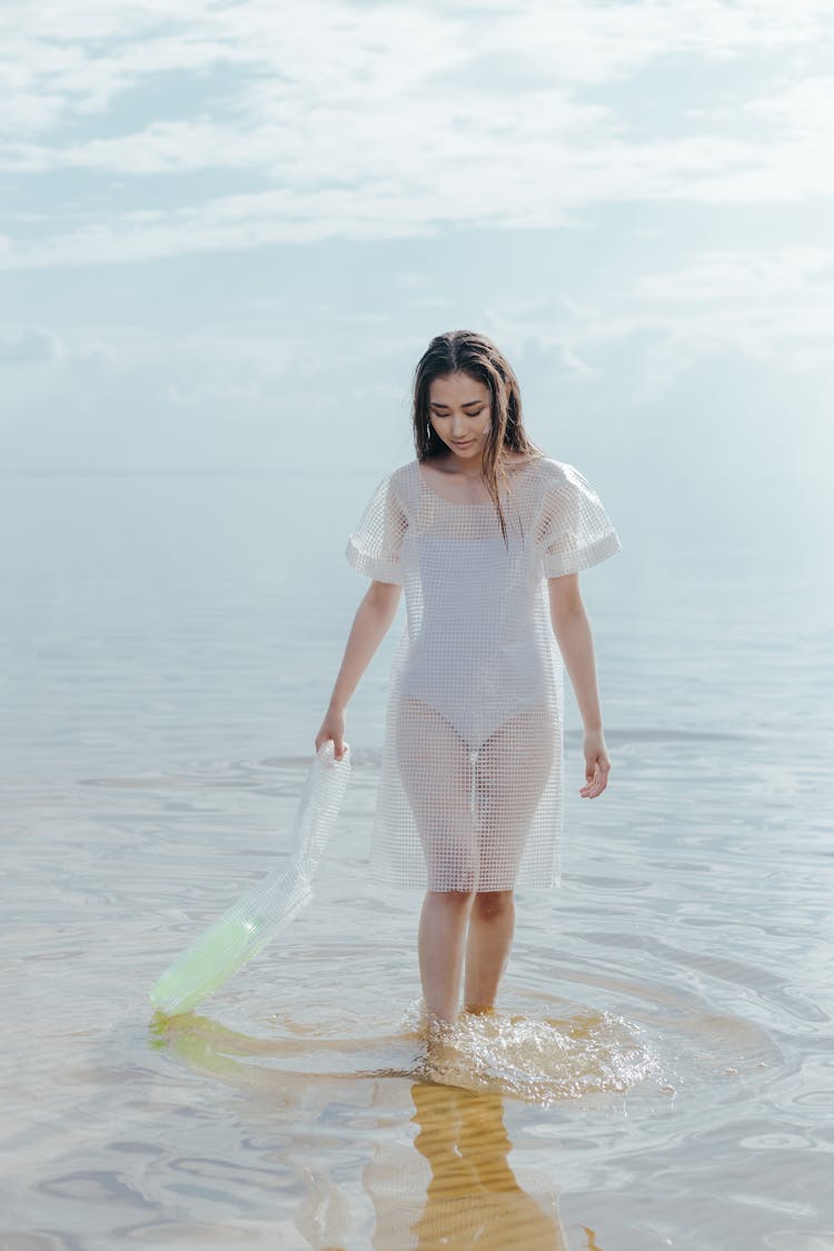 Woman In White Dress Holding A Plastic Bag While In The Water