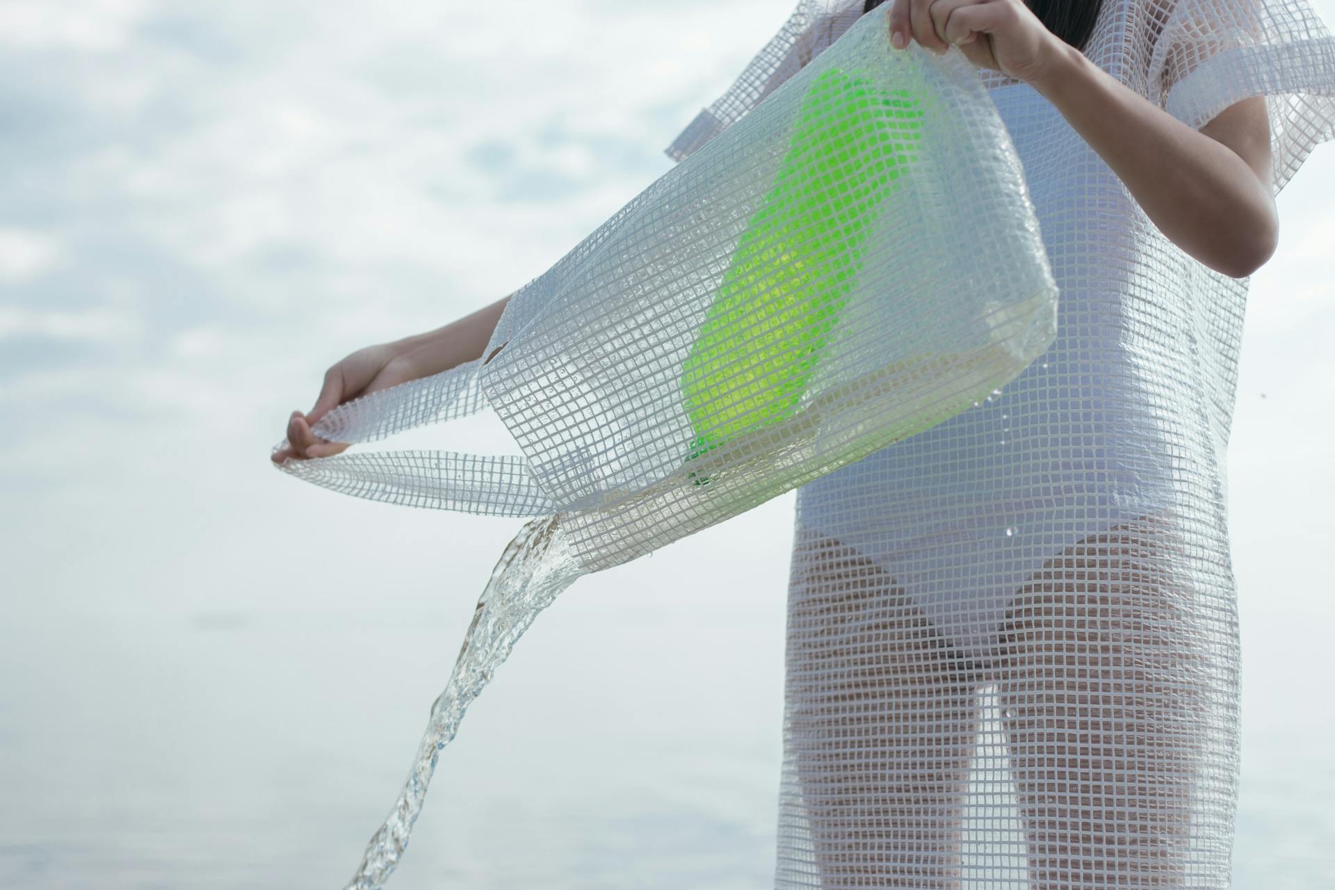 A person pouring water from a mesh bag into the sea, symbolizing eco-friendly practices.