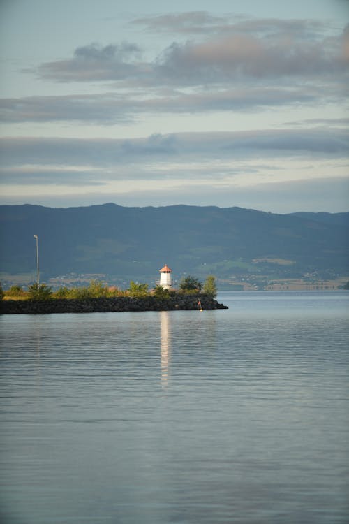 White and Brown Lighthouse Near Body of Water Under Cloudy Sky