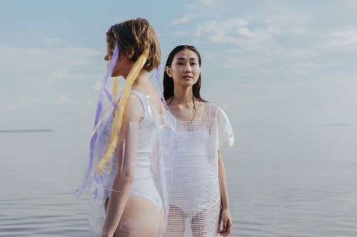 Free Two women stand elegantly by a calm beach in an artistic setting. Stock Photo