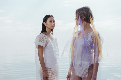 Free Two women in futuristic outfits standing by tranquil water. Stock Photo